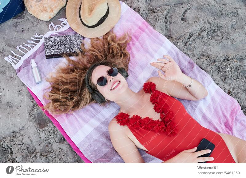 Happy young woman lying on towel on the beach listening to music human human being human beings humans person persons curl curled curls curly hair towels