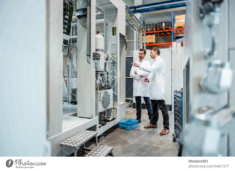 Two men wearing lab coats talking in factory speaking man males Laboratory Coat Labcoats Lab Coat Laboratory Coats Lab Coats factories discussing discussion