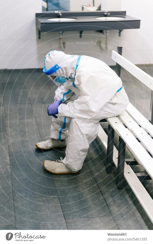 Contemplating man wearing protective suit sitting on bench in hospital color image colour image indoors indoor shot indoor shots interior interior view