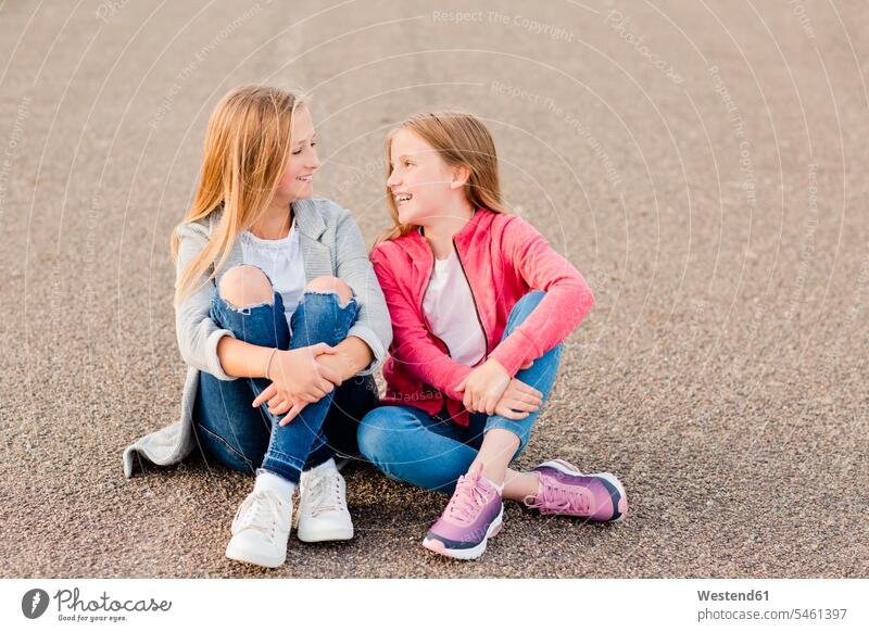 Two smiling girls sitting side by side on the ground land females paralell Juxtaposed in paralell Seated smile child children kid kids people persons