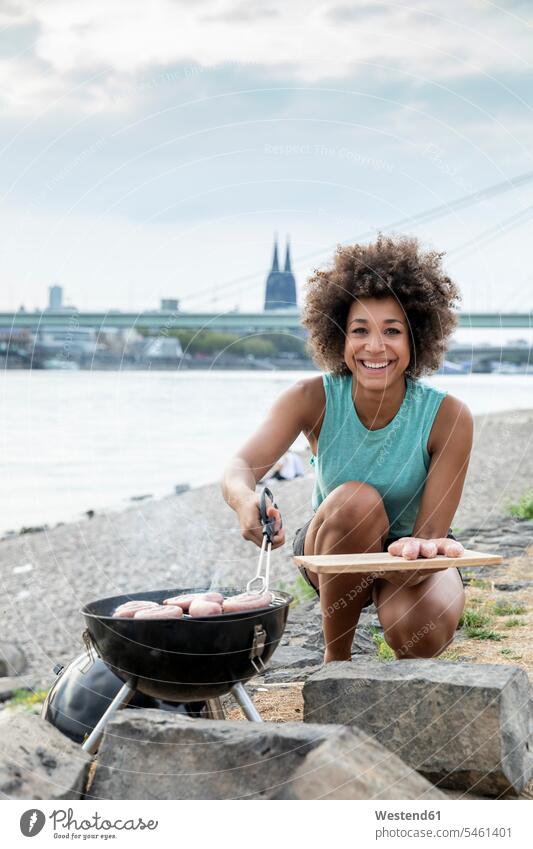 Germany, Cologne, portrait of smiling woman having a barbecue at the riverside smile portraits Barbecue BBQ Barbeque riverbank females women water's edge