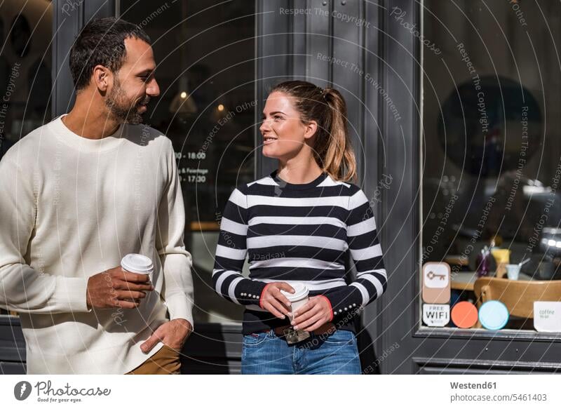 Man and woman holding takeaway cups outside a cafe talking speaking Coffee disposable cup disposable cups couple twosomes partnership couples Drink beverages