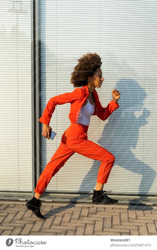 Running young woman with smartphone wearing fashionable red pantsuit human human being human beings humans person persons Mixed Race mixed race ethnicity