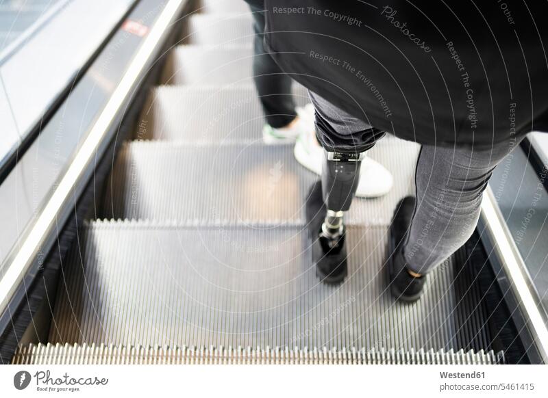 Close-up of woman with leg prosthesis standing on escalator Escalators moving staircase moving stairs mobile on the go on the road on the way back view