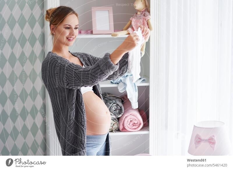 Pregnant woman with baby clothes in baby room body bodies females women children's room Kids Room nursery child's room pregnant Pregnant Woman portrait