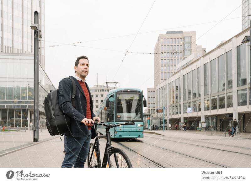 Entrepreneur with bicycle standing against cable car in city, Frankfurt, Germany color image colour image outdoors location shots outdoor shot outdoor shots day