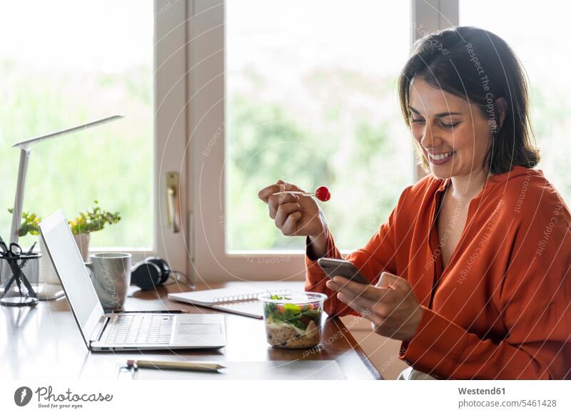 Smiling business person using mobile phone while eating salad at home color image colour image indoors indoor shot indoor shots interior interior view Interiors