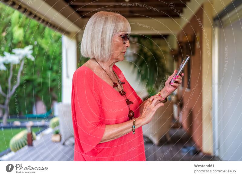 Stylish senior woman using smart phone while standing at patio color image colour image Spain leisure activity leisure activities free time leisure time