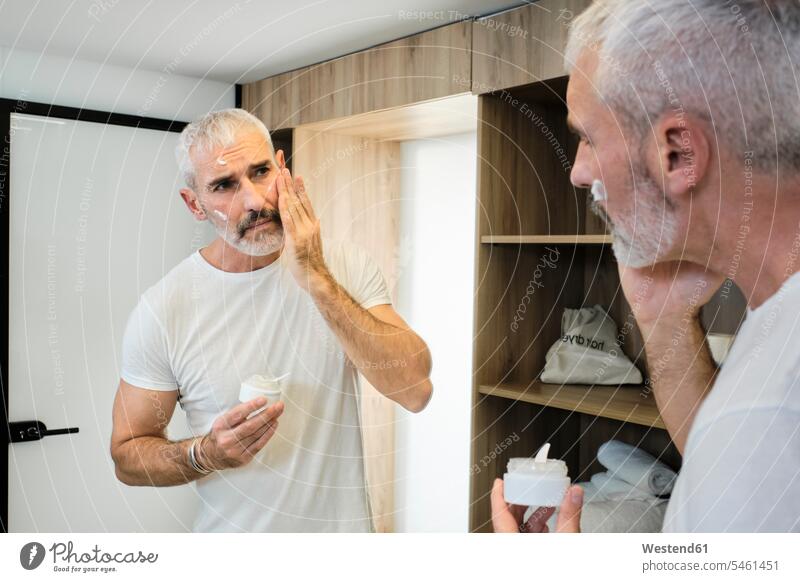 Mature man applying face cream while looking in mirror at bathroom color image colour image indoors indoor shot indoor shots interior interior view Interiors