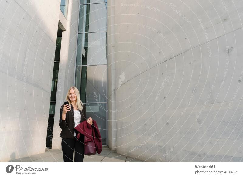 Blond businesswoman using smartphone in the background modern buildings business life business world business person businesspeople business woman