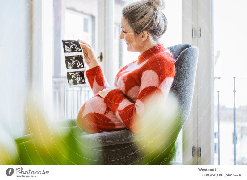 Pregnant woman holding ultrasound image at home human human being human beings humans person persons caucasian appearance caucasian ethnicity european 1