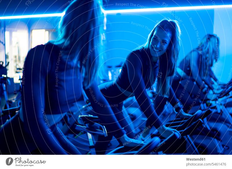 Smiling twin sisters exercising on spinning bikes in gym human human being human beings humans person persons caucasian appearance caucasian ethnicity european