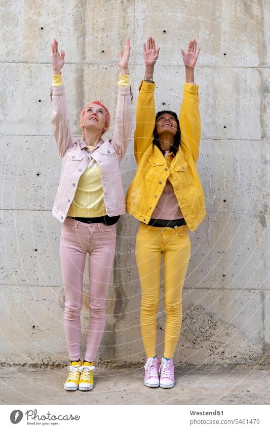Two alternative friends wearing yellow and pink jeans clothes, posing, raising arms female friends Alternative homosexual queer same-sex homosexually gay pose