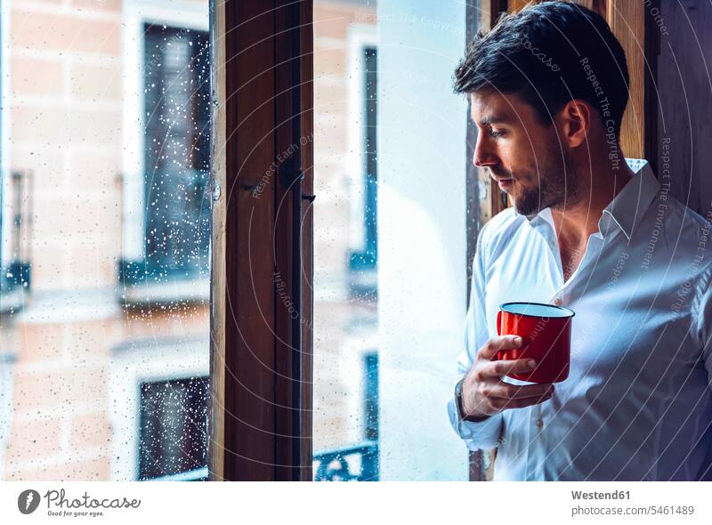 Young man holding cup looking out of window human human being human beings humans person persons celibate celibates singles solitary people solitary person