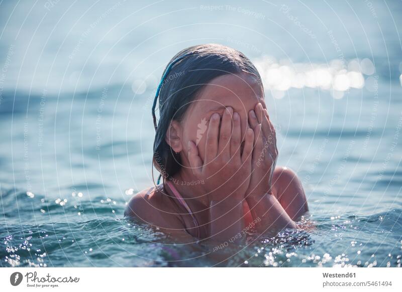 Girl covering face with hand while playing in sea during summer color image colour image outdoors location shots outdoor shot outdoor shots day daylight shot