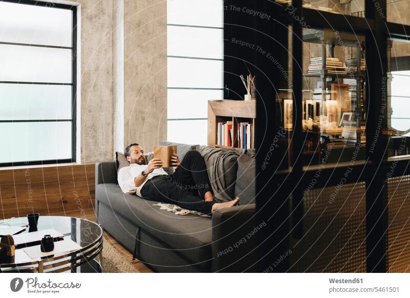 Mature man lying on couch, relaxing, reading book human human being human beings humans person persons caucasian appearance caucasian ethnicity european 1