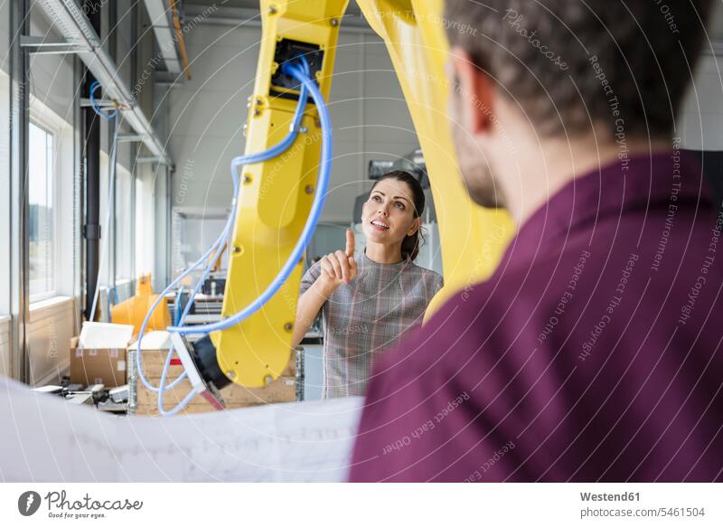 Businessman and woman having a meeting in front of industrial robots in a high tech company firm high-tech maintenance manufacturing checking Test testing Check