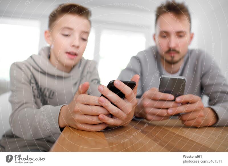 Young man and teenager using smartphones in a living room telecommunication telephone telephones cell phone cell phones Cellphone mobile mobile phones mobiles
