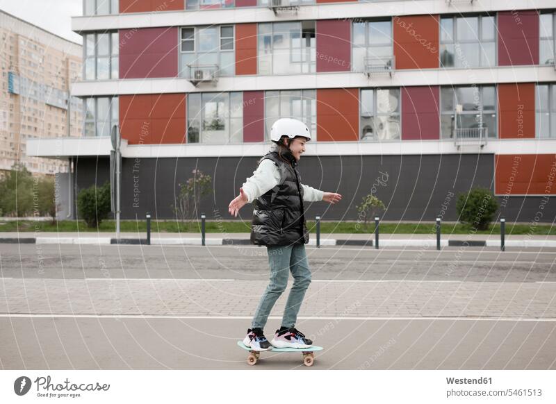 Girl wearing warm clothing skateboarding on road against building color image colour image leisure activity leisure activities free time leisure time outdoors