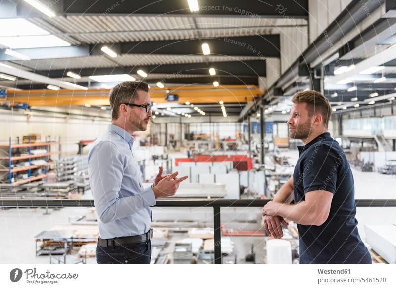 Two men talking on factory shop floor speaking production hall factories man males colleagues Adults grown-ups grownups adult people persons human being humans