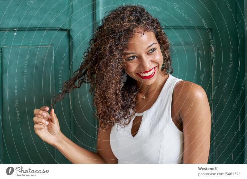 Portrait of smiling young woman with curly hair in front of green wooden door smile toothy smile big smile open smile laughing head cocked strand of hair