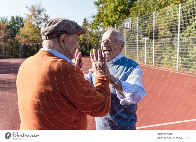 Two fit seniors high fiving on a basketball field High Five Hi-Five high-fiving High-Five sportive sporting sporty athletic playing fitness basketball ground