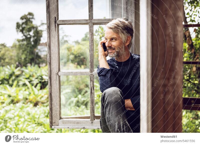 Man on cell phone sitting in the window in tropical surrounding Indonesia recreation relaxing Recreational wooden listening wireless Wireless Connection