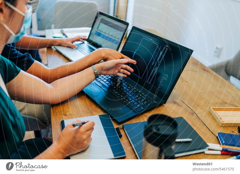 Programmers discussing over laptop while wearing protective face mask at office during coronavirus color image colour image indoors indoor shot indoor shots
