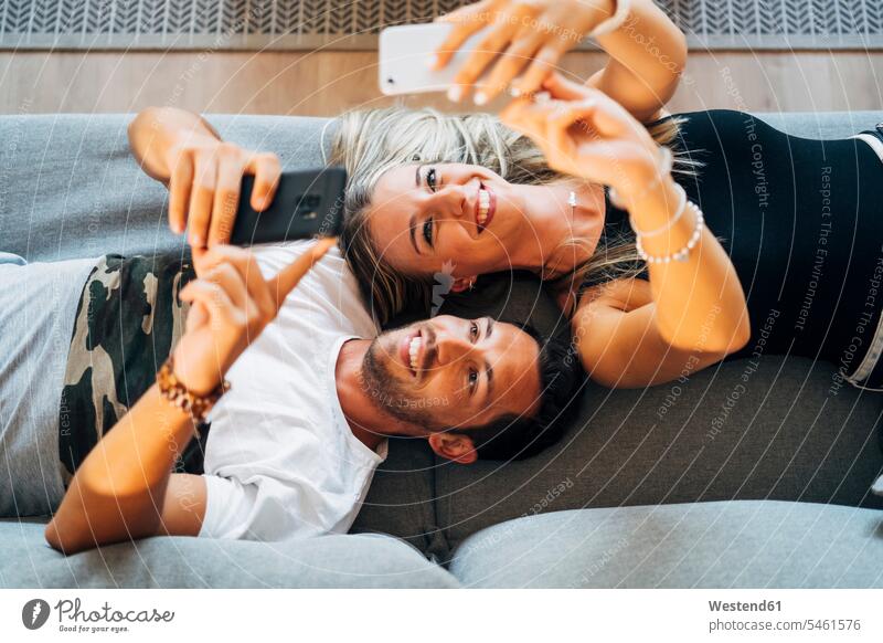 Portrait of laughing couple lying on the the couch taking selfies with smartphones human human being human beings humans person persons caucasian appearance