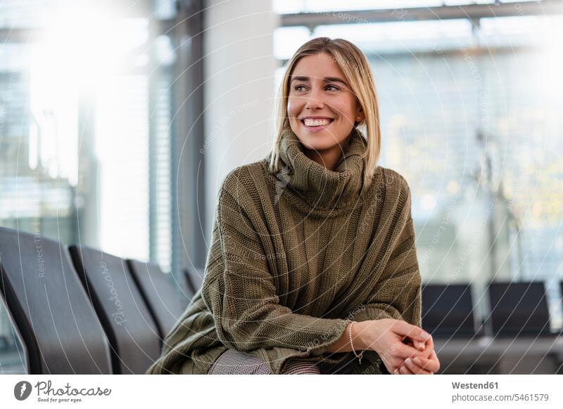 Smiling young woman sitting in waiting area looking around smile travel traveling Seated relax relaxing relaxation delight enjoyment Pleasant pleasure