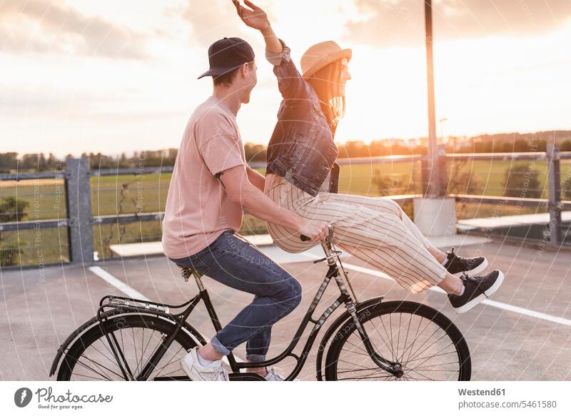 Happy young couple together on a bicycle on parking deck at sunset hats bikes cycles bicycles Seated sit in the evening Ardor Ardour enthusiasm enthusiastic