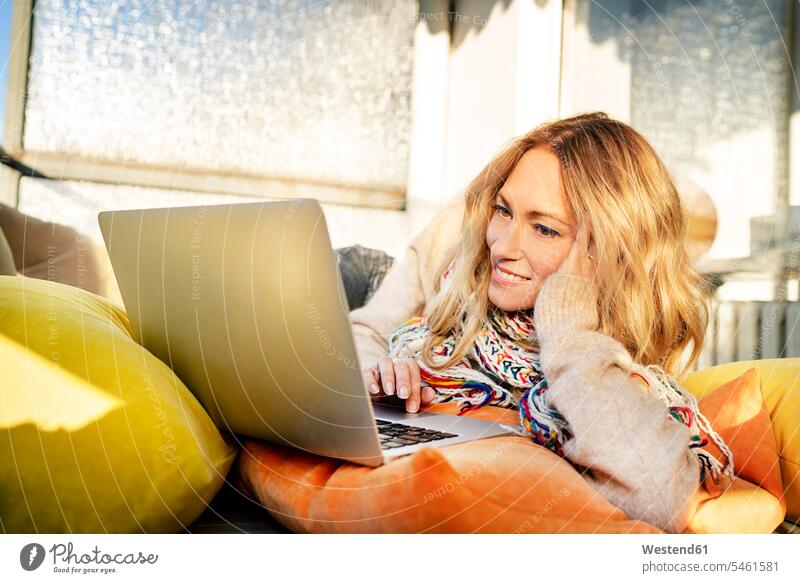 Portrait of smiling blond mature woman relaxing in winter garden using laptop females women winter gardens conservatory Sun Room Sunroom portrait portraits use