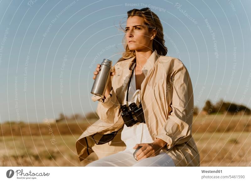 Female traveller with binoculars drinking thermos flask discover discovering Seated sit hike thirsty explore exploring free Liberty free time leisure time