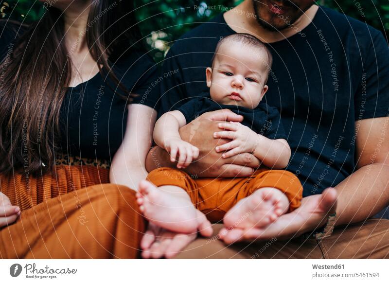 Cute baby boy sitting on father's lap by mother at park color image colour image Portugal outdoors location shots outdoor shot outdoor shots day daylight shot