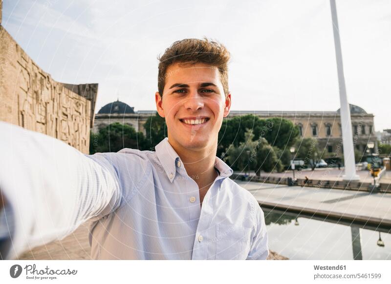 Smiling handsome young man taking selfie in city against clear sky color image colour image Spain outdoors location shots outdoor shot outdoor shots day