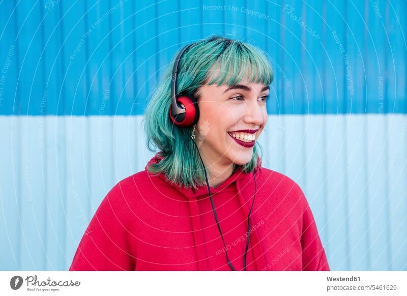 Portrait of laughing young woman with blue dyed hair listening music with headphones headset Laughter portrait portraits females women coloured hearing positive