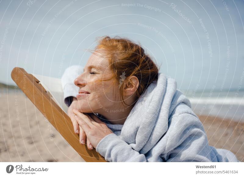Smiling woman lying in deck chair, enjoying sunbath at the beach deckchair deckchairs deck chairs beaches females women indulgence enjoyment savoring indulging