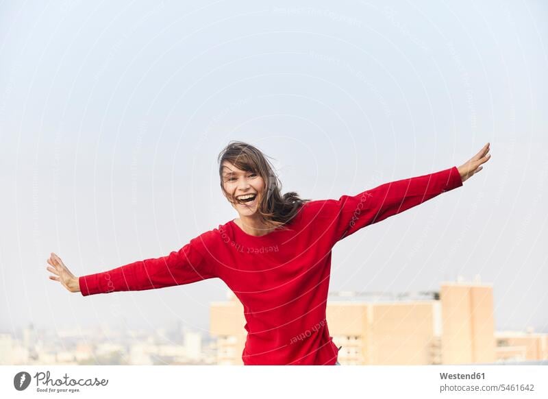 Mature woman laughing with arms outstretched while standing on building terrace against clear sky color image colour image outdoors location shots outdoor shot