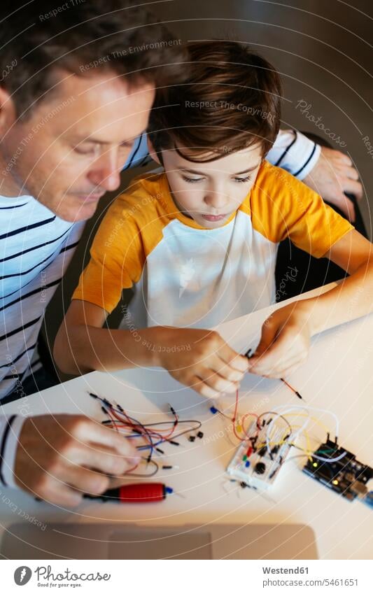 Father and son assembling an electronic construction kit electric electrical sons manchild manchildren assembly set father pa fathers daddy dads papa assemble