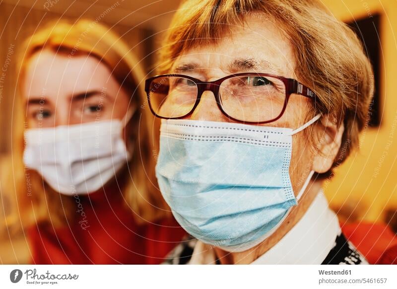 Grandmother wearing face mask and eyeglasses staring while sitting by granddaughter at home color image colour image day daylight shot daylight shots day shots
