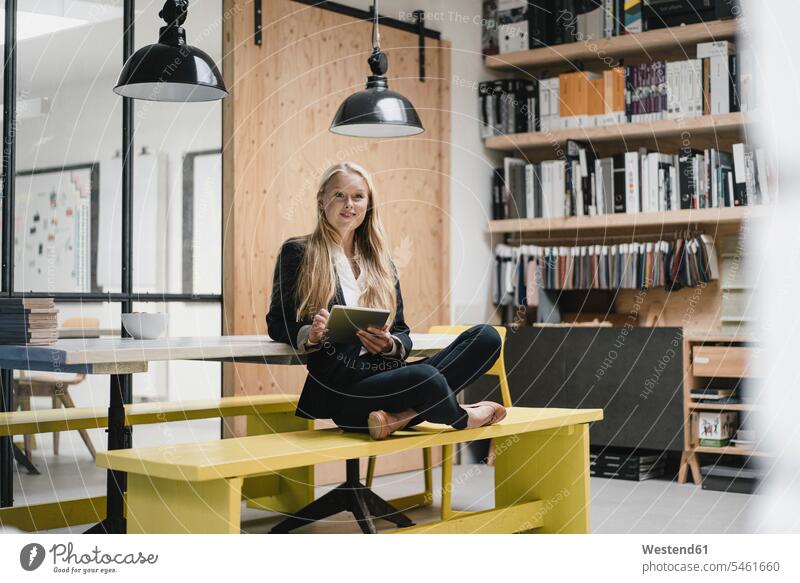 Young businesswoman sitting on a bench in a loft office using a tablet Occupation Work job jobs profession professional occupation business life business world
