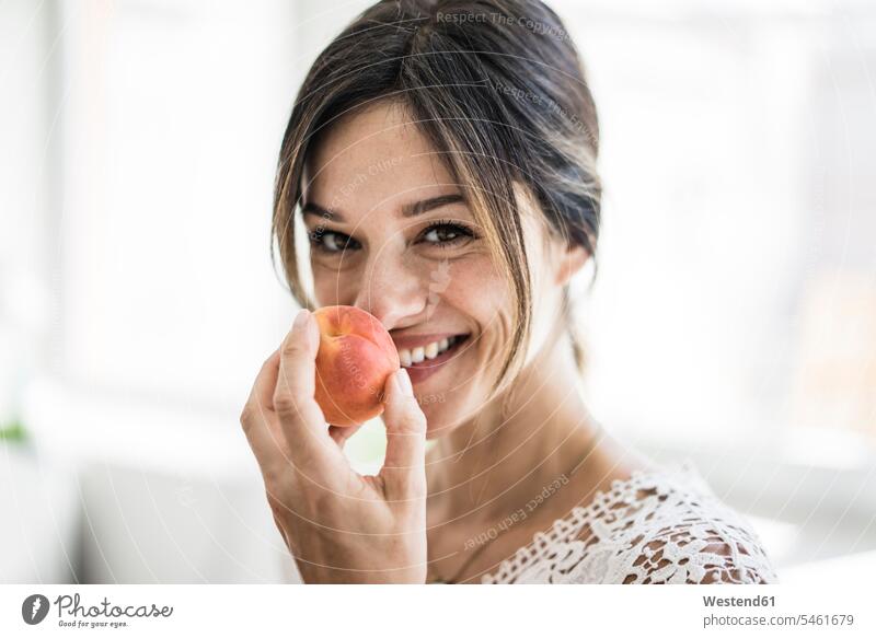 Laughing woman smelling an apricot kitchen domestic kitchen kitchens aroma flavour aromatic apricots Healthy Food holding mature woman mature women Fruit Fruits