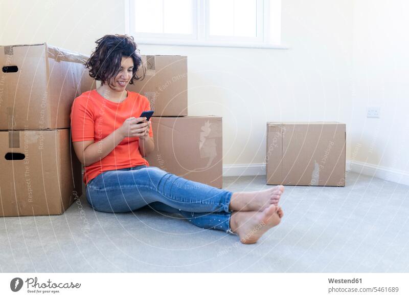 Woman sitting on the floor in new home using cell phone cardboard cardboard boxes Cardboard Carton Cardboards cardbox cardboxes carton cartons windows T- Shirt