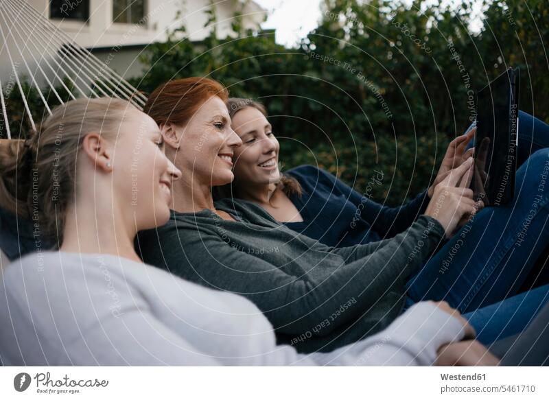 Happy mother with two teenage girls lying in hammock in garden in autumn using tablet digitizer Tablet Computer Tablet PC Tablet Computers iPad Digital Tablet