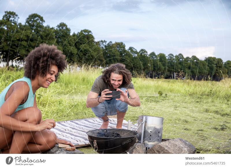 Smiling young man with girlfriend taking a picture of barbecue grill in the nature photographing smiling smile natural world couple twosomes partnership couples