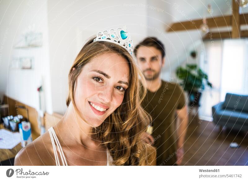 Portrait of smiling woman wearing tiara at home with man in background portrait portraits diadem Tiaras coronet couple twosomes partnership couples smile people