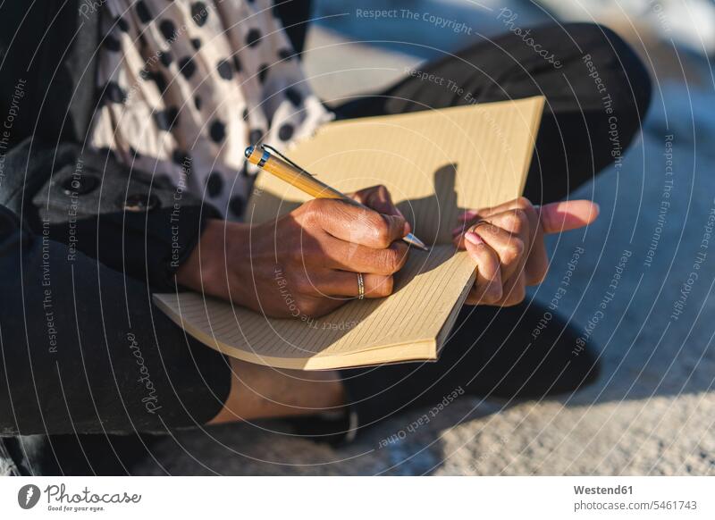 Woman sitting on a wall writing in notebook, close-up write notebooks Seated woman females women walls Adults grown-ups grownups adult people persons