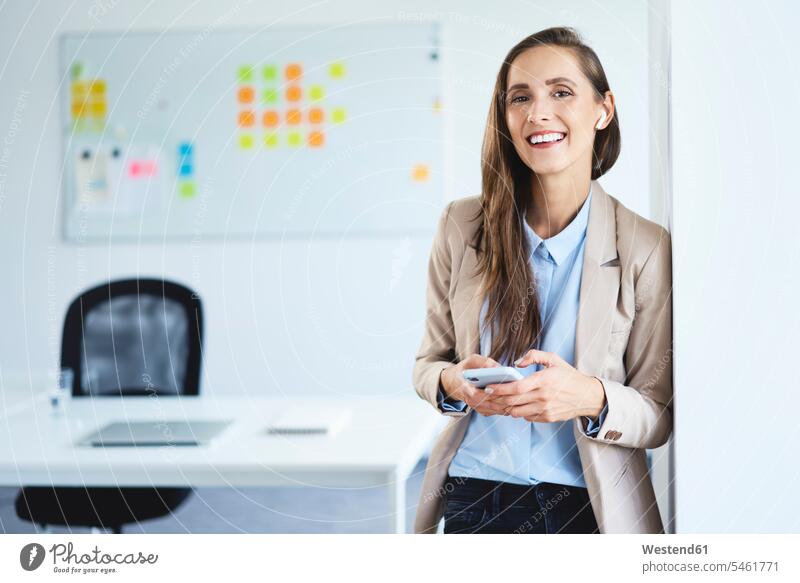 Young businesswoman standing in office holding phone and smiling at camera Occupation Work job jobs profession professional occupation business life