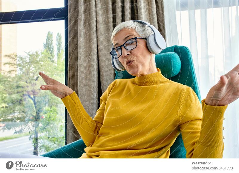 Senior woman sitting in armchair, listening music with headphones Curtains Draperies Drapery windows jumper sweater Sweaters chairs Arm Chair Arm Chairs