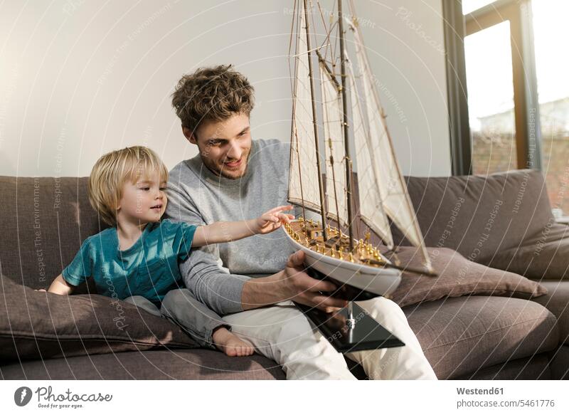 Father and son looking at toy model ship on couch at home sons manchild manchildren settee sofa sofas couches settees sitting Seated model boat father pa